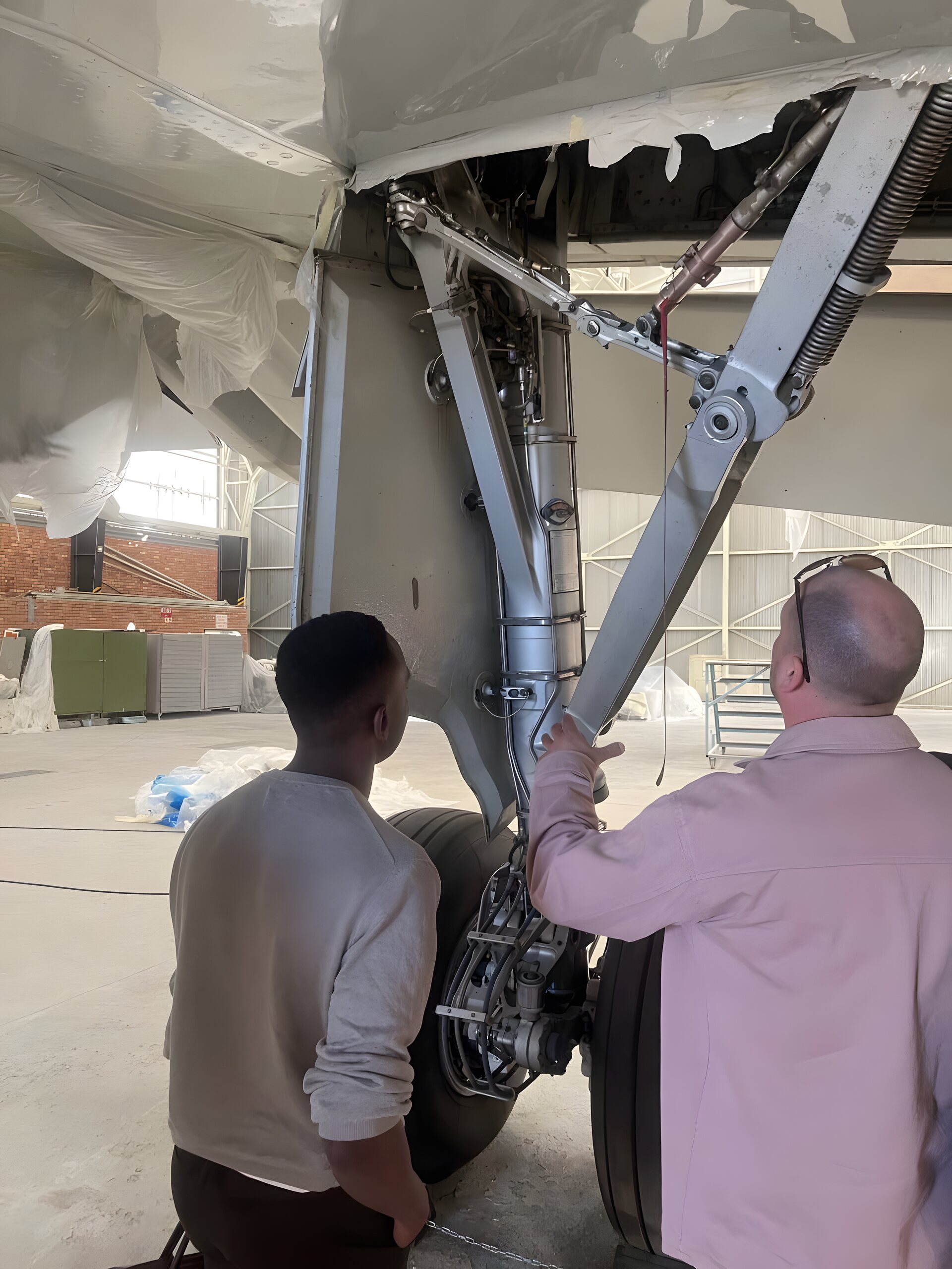 Two Ubunye engineers inspect a main landing-gear assembly in the hangar